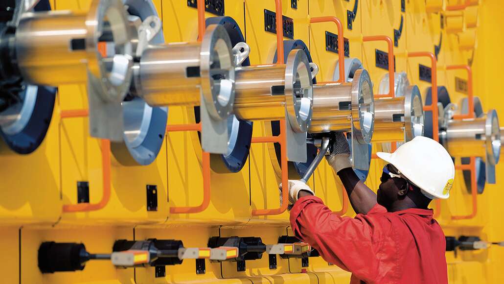 ExxonMobil employee wearing a white hard hat and red uniform inspecting metal onsite